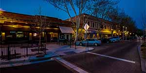 Nighttime view of downtown Tracy with illuminated restaurants, shops, and parked cars along a quiet brick-paved street