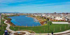 Modern neighborhood in Lathrop, CA featuring a serene blue lagoon, walking paths, and landscaped green spaces for families