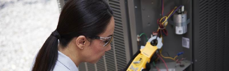 HVAC technician using a manifold gauge to repair an outdoor AC unit.