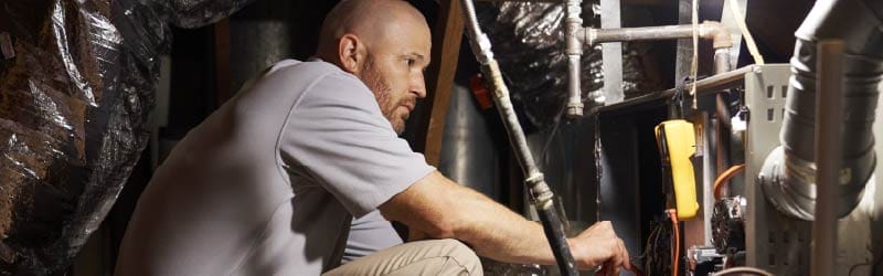 HVAC technician repairing a residential furnace in a crawl space.